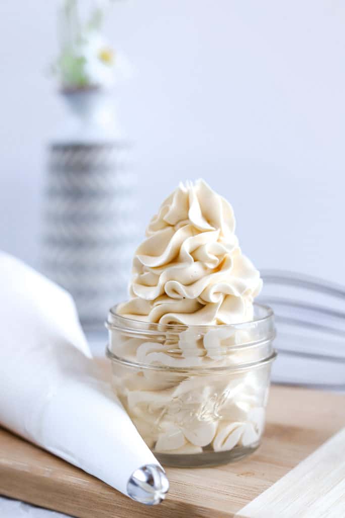 A mason jar with a swiss meringue buttercream swirl next to a piping bag