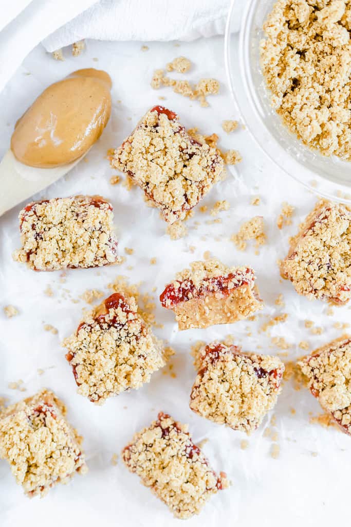Peanut butter and jelly bars with a streusel topping with a wooden spoon of peanut butter