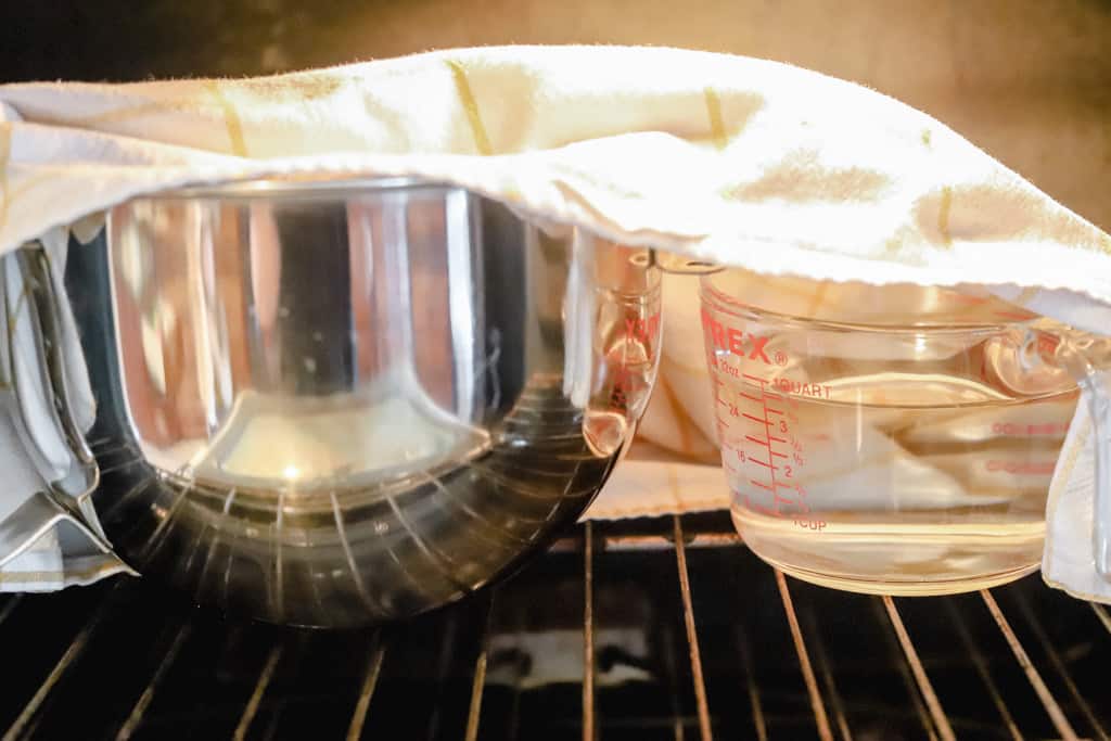 A bowl of dough rising in the oven with a bowl of boiling water