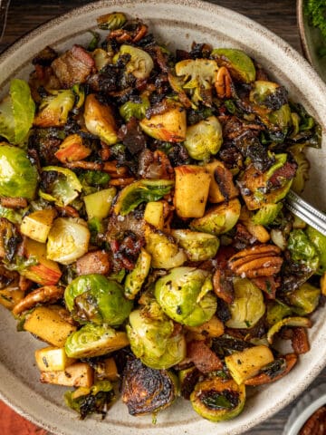 An overview shot of a bowl of brussel sprouts with apples and pecans topped with balsamic glaze.