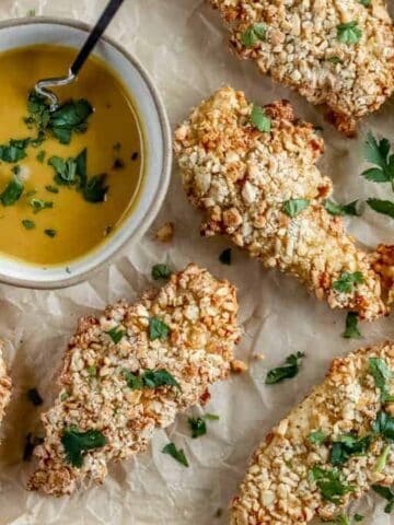 A pan of cashew crusted chicken tenders next to a bowl of honey mustard dipping sauce