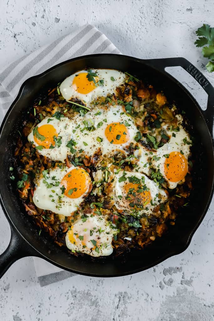 A top shot of hashbrowns and eggs in a cast iron skillet on a grey background