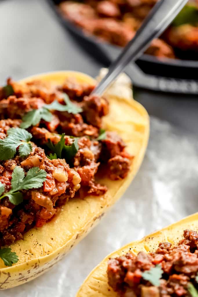 A close up view of a spaghetti squash half filled with whole30 meat sauce on a white background
