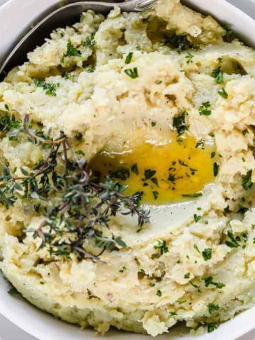 A bowl of mashed sweet potatoes topped with fresh herbs and melted ghee