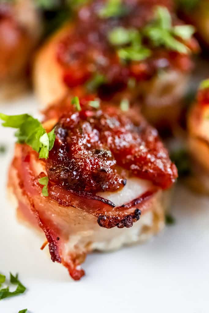 A scallop wrapped in bacon topped with sweet pepper relish.