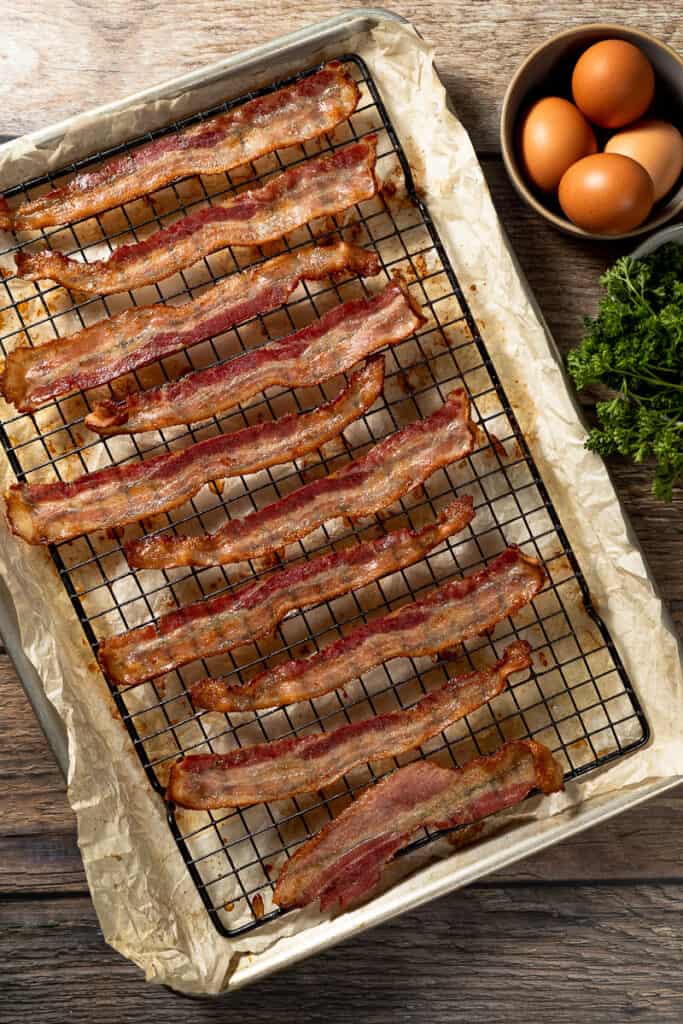 A baking sheet with cooked crispy oven bacon on a wood background
