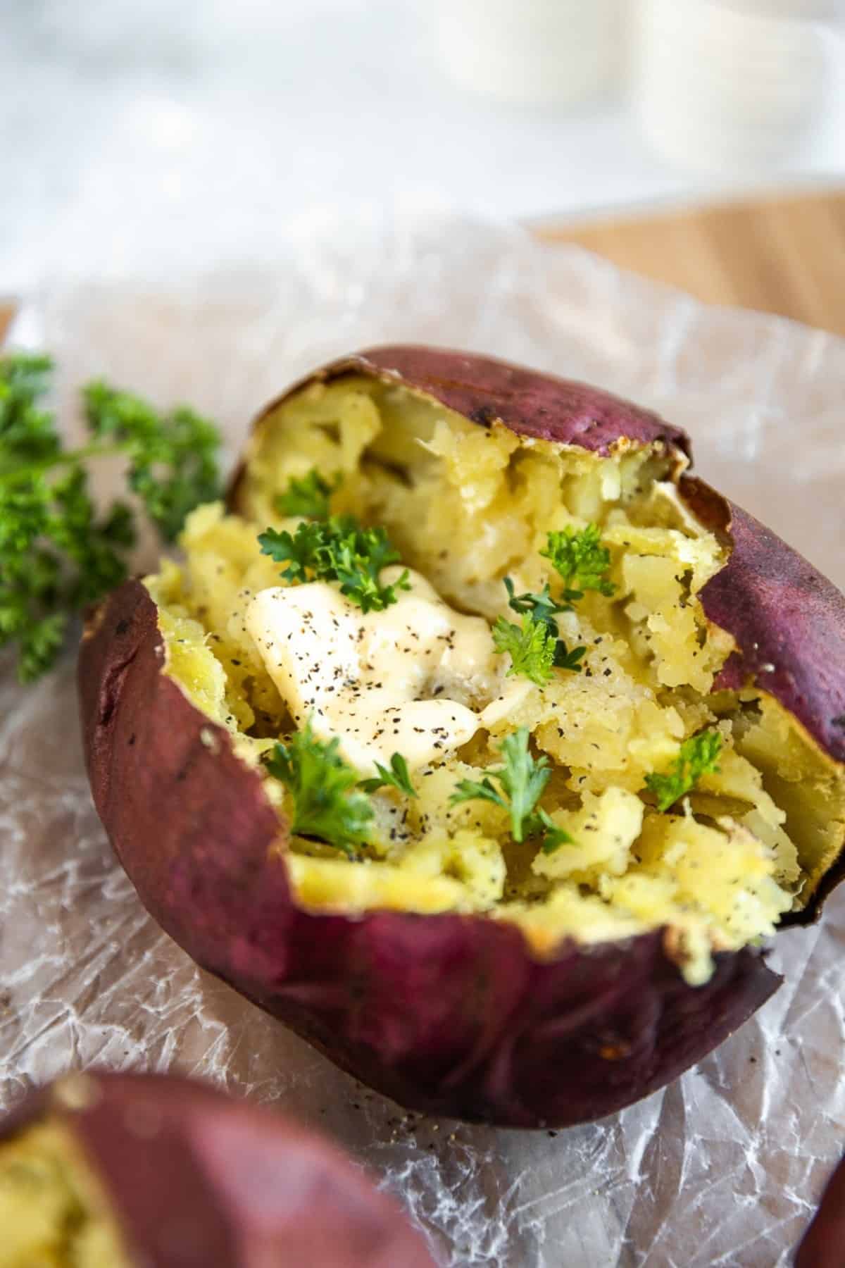 An overview shot of a baked sweet potato topped with butter and parsley