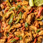 An overhead closeup shot of chicken fajitas on a pan topped with chopped cilantro and lime wedges.