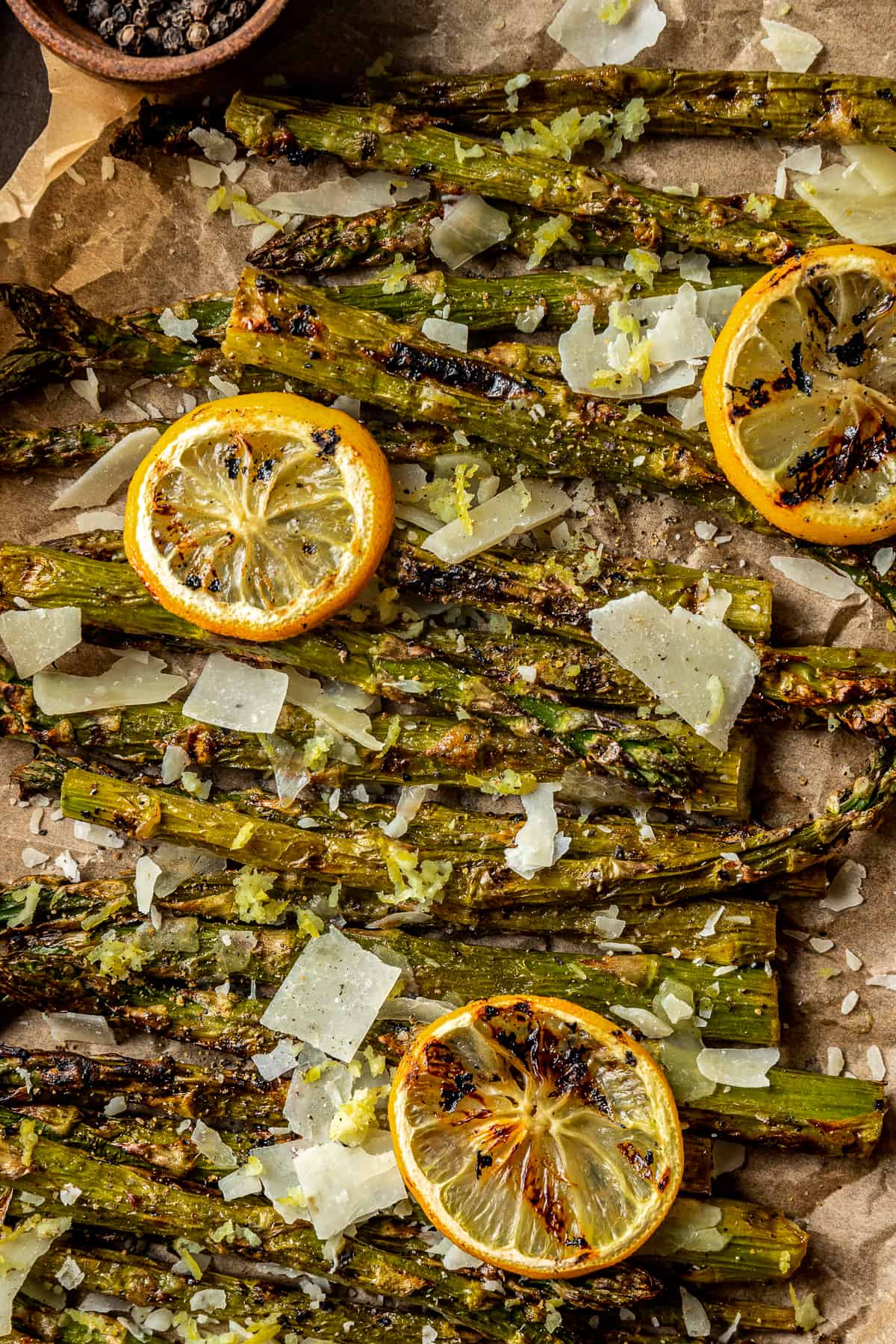 An overview shot of grilled asparagus spears topped with grilled lemon, parmesean cheese, and cracked black pepper.