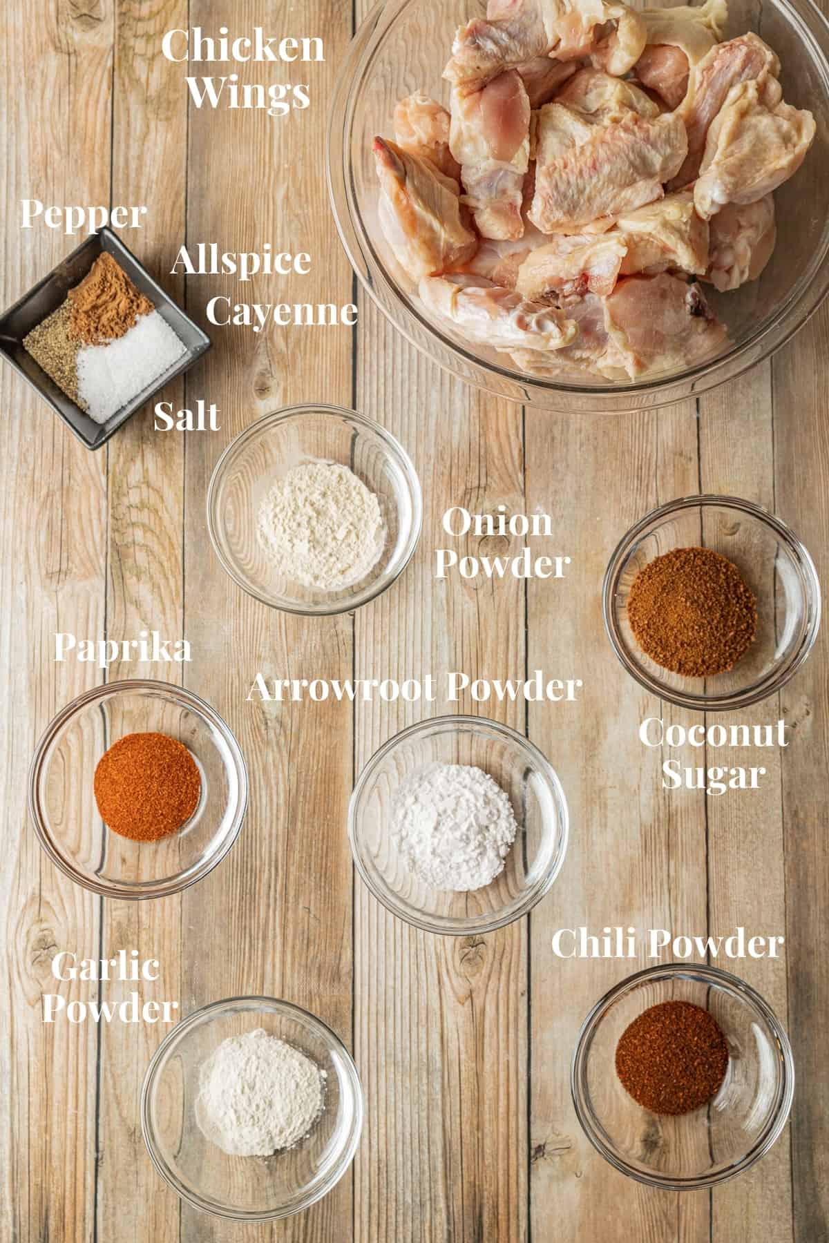 The ingredients needed for dry rub chicken wings in glass bowls on a wood background.