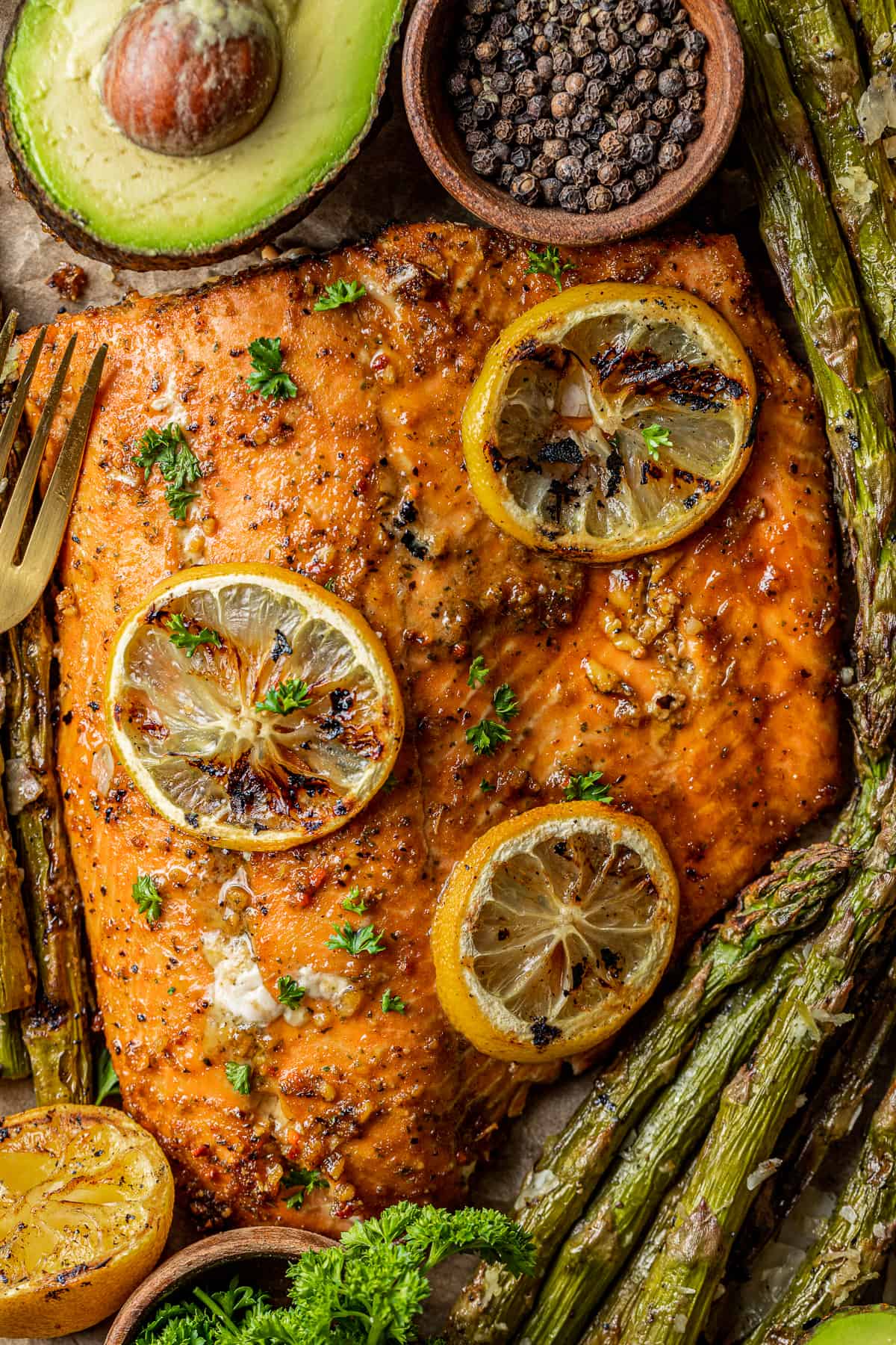 An overview shot of a whole salmon fillet topped with lemon and served with roasted asparagus.