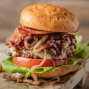 Two smash burger patties between a hamburger bun topped with lettuce, tomato, bbq sauce, and onions.