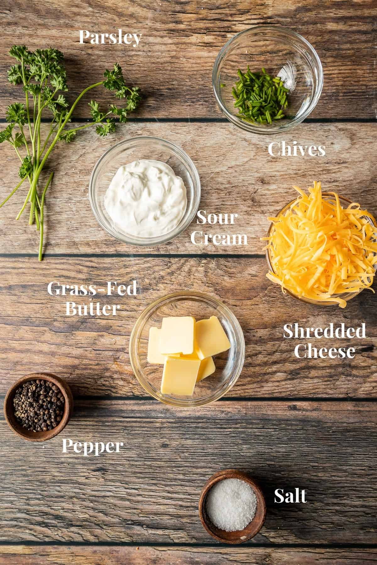 An overview shot of popular baked potato toppings in glass bowls on a wood background.
