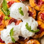 Smoked peaches with grill marks on a baking sheet topped with vanilla ice cream and mint leaves.