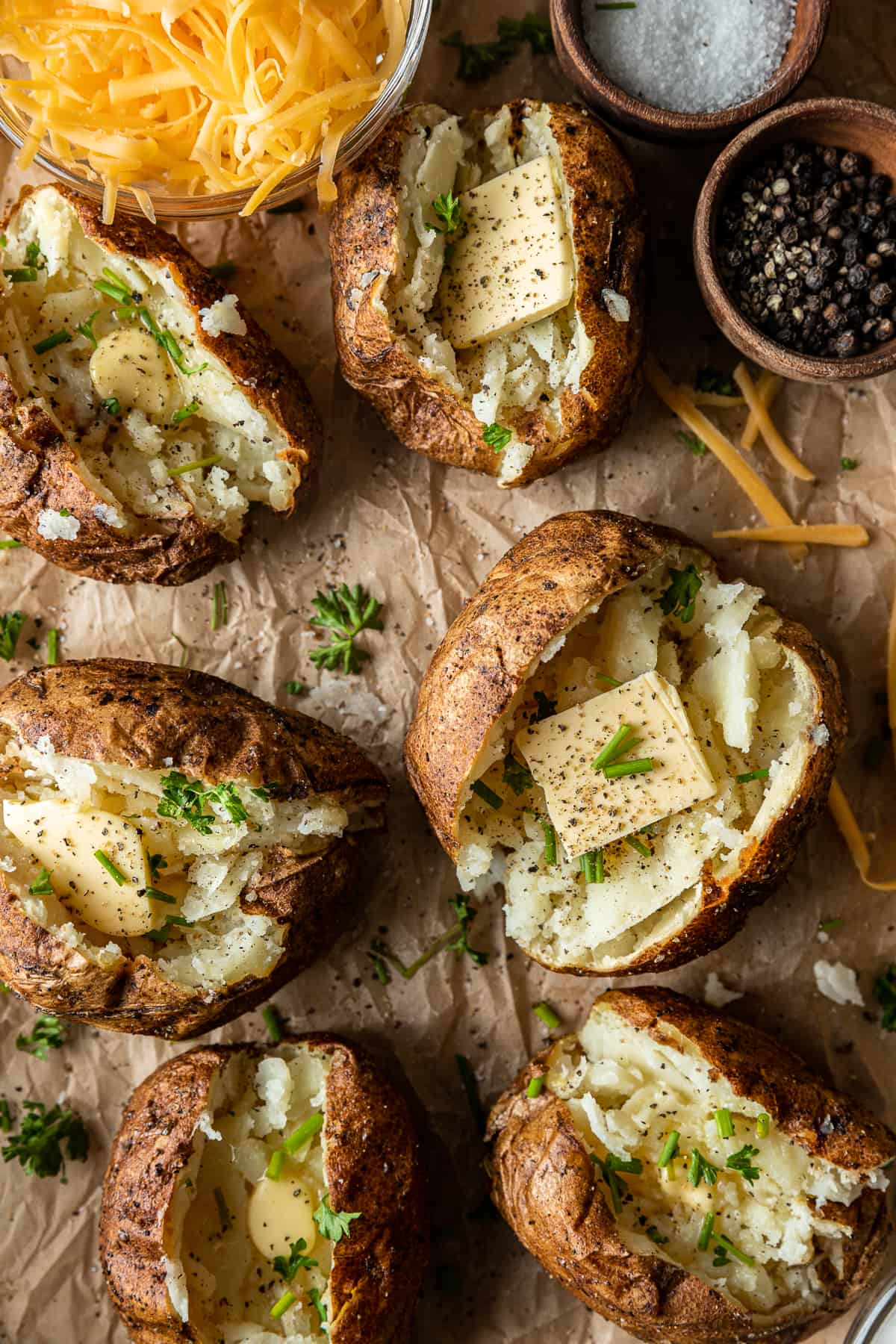 An overview shot of baked potatoes sliced open and topped with butter and salt and pepper.