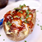 A twice baked brisket potato topped with bbq sauce and herbs on a white background.